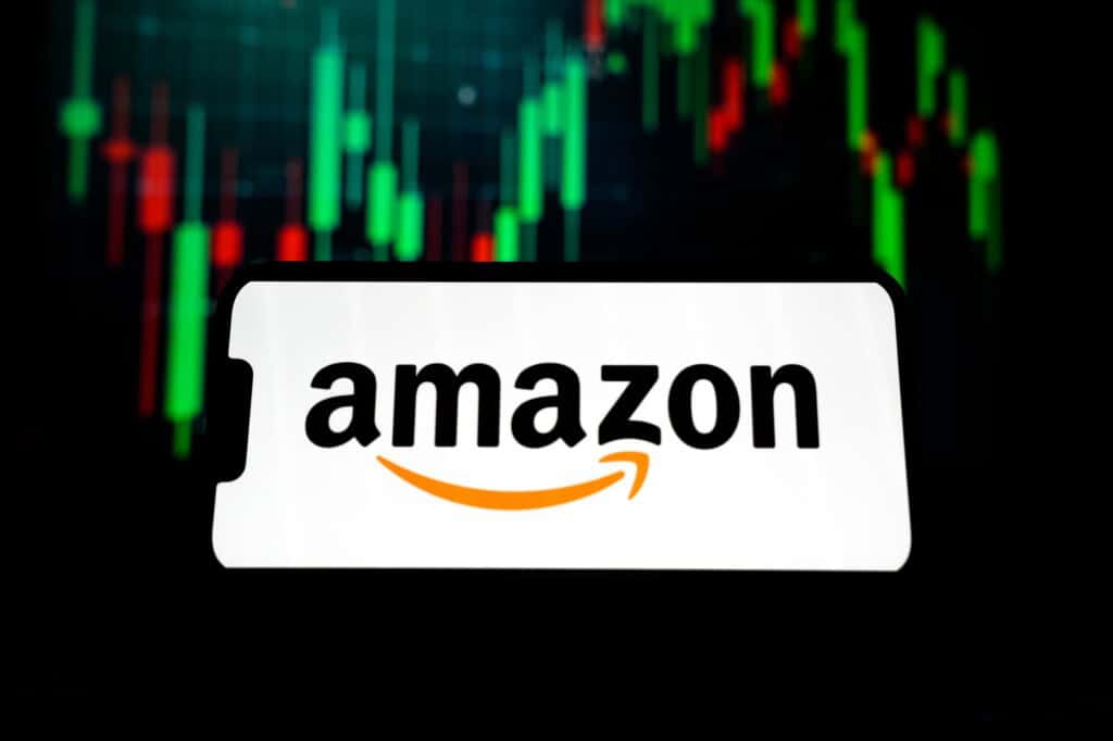 Ao fundo, gráficos financeiros; à frente, logo da Amazon na tela de um smartphone