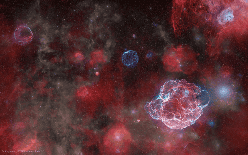 Imagem de longa exposição revela, em cores, a vasta constelação do Cocheiro. Nuvens de hidrogênio (vermelho), oxigênio (azul) e poeira abrigam remanescentes de supernovas, verdadeiros “fantasmas cósmicos” de estrelas que explodiram há milên