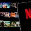 Ao fundo, desfocado, tela inicial da Netflix em uma TV; à frente, celular com o logo da empresa na tela