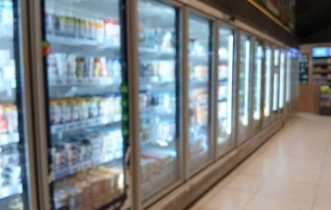 Corredor de supermercado com geladeiras e freezers expositores alinhados, com portas de vidro e produtos refrigerados nas prateleiras.