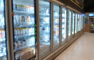 Corredor de supermercado com geladeiras e freezers expositores alinhados, com portas de vidro e produtos refrigerados nas prateleiras.